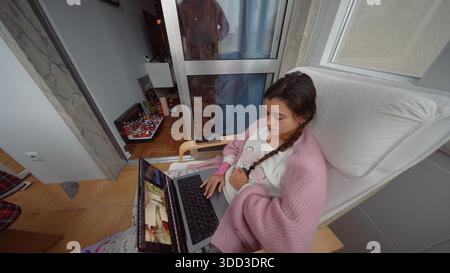 Lady in pink dress concentrates on image editing outside on balcony Stock Photo