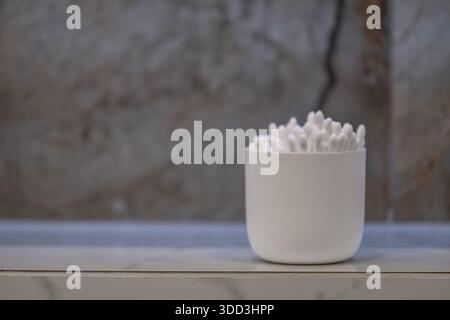 Cotton Swabs in Minimal White Container on Shelf Against Neutral Wall Background Stock Photo
