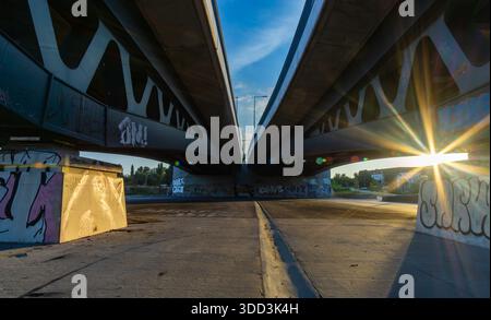 Symmetrical view beneath two parallel road bridges in Berlin, Germany, photographed during golden hour. Under a bridge, sunstar, editorial. Stock Photo