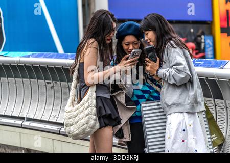 Three young women look at a smartphone and a camera in Osaka, Osaka Prefecture, Japan Stock Photo