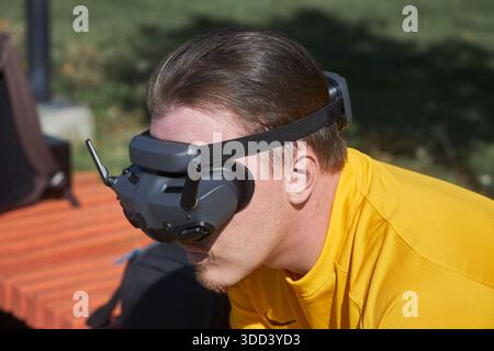 Man with brown hair wearing drone FPV goggles outdoors for remote flying experience. Technology and virtual reality for recreation. Stock Photo