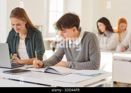 Focused young university students sitting at desk in classroom, writing notes, engaged in learning. Stock Photo