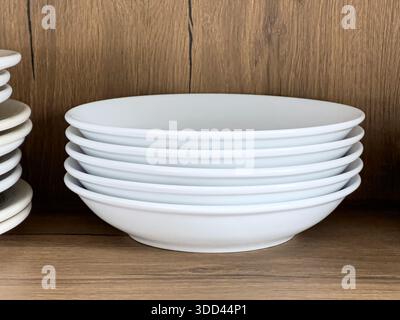 White ceramic bowls are stacking neatly on a wooden shelf in a kitchen cabinet Stock Photo
