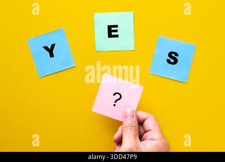 Hand holding sticky note with question mark next to yes spelling sticky notes Stock Photo