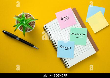 Sticky notes displaying goal, motivation, and success on a notebook with a pen and plant Stock Photo