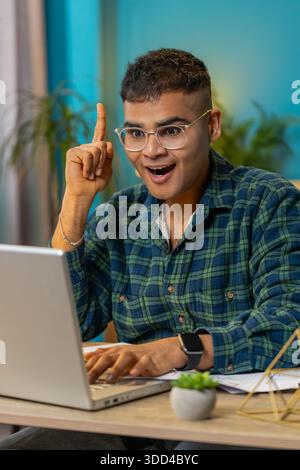 Eureka. Thoughtful inspired Indian man working on laptop make gesture raises finger came up with creative plan feels excited with good idea inspiration motivation, question at home office. Vertical Stock Photo