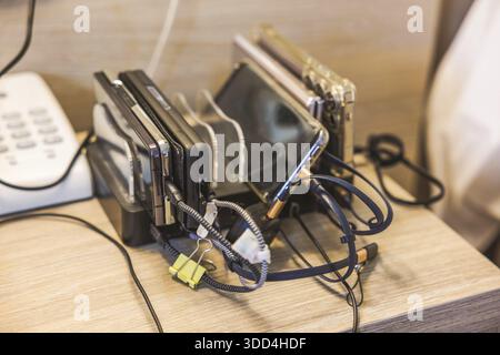 Close up view of charging station with multiple smartphones and cables on hotel bedside table. Greece. Stock Photo