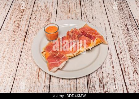 A magnificent slice of toast with Serrano ham, tomato and oil on a simple white porcelain plate Stock Photo
