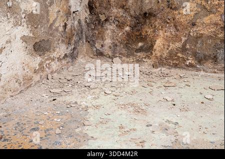 A corner of a room with peeling paint and cracked plaster on walls and floor. Stock Photo