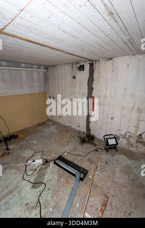 A basement with exposed concrete walls, a crack filled with sealant, and construction tools on the floor. Stock Photo