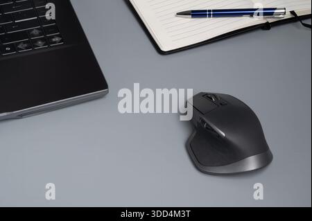 A modern office setup with a laptop, wireless mouse, notebook, and pen on a gray desk. Stock Photo