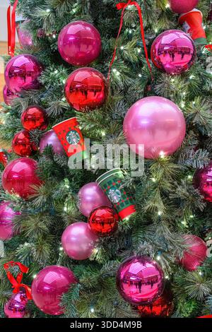 Close-up of a Christmas tree decorated with pink and red ornaments, lights, and Starbucks holiday cups. Stock Photo