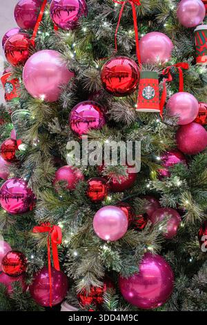 Close-up of a Christmas tree decorated with pink and red ornaments, lights, and holiday cups. Stock Photo