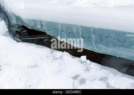 closeup blue ice underside with texture, translucent layers revealing trapped air lines and subtle wave patterns, thin melt channel exposing dark flow Stock Photo