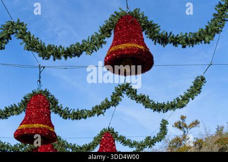 Red Christmas bell decorations hanging with green garland against blue sky Stock Photo
