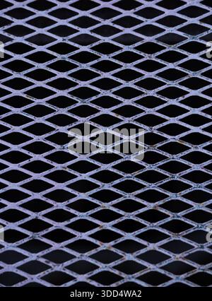 vertical image of metal grate with diamond shapes silver grey metal with black background connecting lines crossing each other protective fence grill Stock Photo