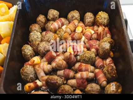 Roasting tray filled with pigs in blankets and seasoned stuffing balls prepared for a traditional holiday or festive meal Stock Photo