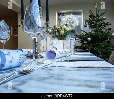 Elegant Christmas dining table set with glassware, festive decorations and a decorated tree in a modern indoor setting Stock Photo