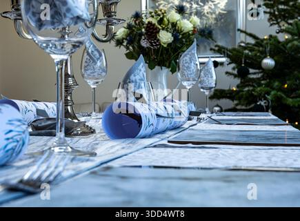 Elegantly decorated dining table set for Christmas with festive napkins, glassware, silverware, and a Christmas tree in the background Stock Photo