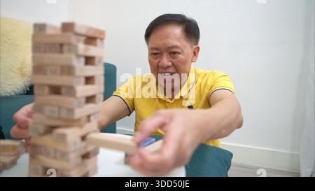 On a holiday, an elderly man enjoys a jenga game in living room of house || Model released Stock Photo