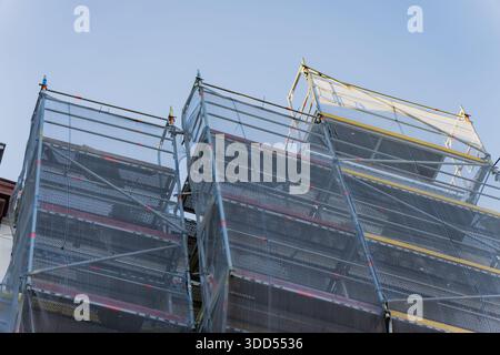 Construction scaffolding towers with safety netting and metal platforms rising against clear sky during facade renovation work on urban building Stock Photo