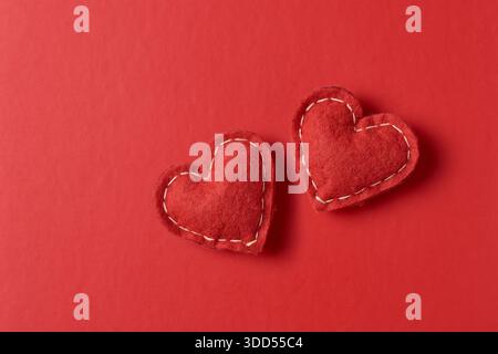 two stuffed red felt hearts on red background, monochromatic color fuzzy fabric texture with soft shadows, minimalist valentine's day romantic Stock Photo