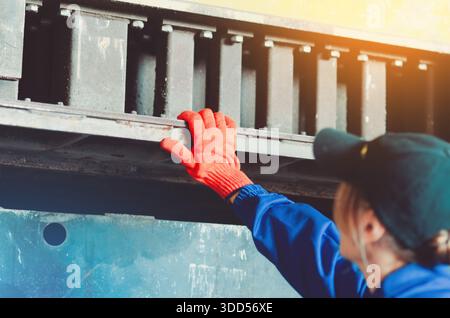 Worker woman in protective blue suit and orange gloves checks strength of equipment. Working in warehouse of production facility. Industrial backgroun Stock Photo