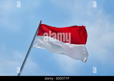 The flag of the Republic of Indonesia, called the red and white flag, flutters gracefully in the blue sky Stock Photo