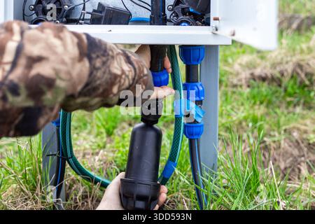 The hands of a person working on installing a water filter connected to a central system of pipes and fittings in a cabinet for automatic drip irrigat Stock Photo