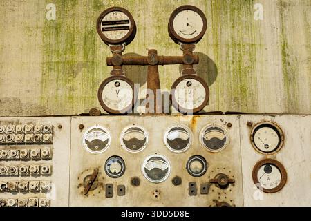 A wall with a bunch of dials and gauges on it. The gauges are old and rusted Stock Photo