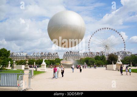 Louvre Museum courtyard in Paris featuring the iconic glass pyramid and a large metallic sphere art installation, with tourists and visitors walking i Stock Photo