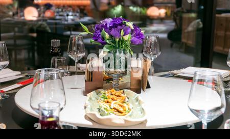 Lxury restaurant round table set for group dining with wine glasses, purple flower centerpiece and Turkish tea creating elegant atmosphere Stock Photo