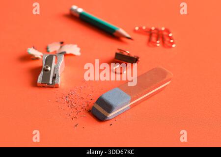 Eraser with pencil, sharpener and paper pins on orange background Stock Photo