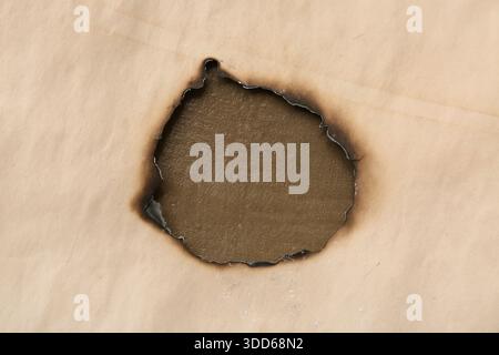 Burned hole in old paper sheet on grunge background, closeup Stock Photo