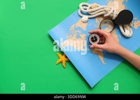 Female hand with modern compass, magnifier, rope and world map on green background Stock Photo