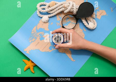 Female hand with modern compass, magnifier, rope and world map on green background Stock Photo
