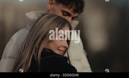 A romantic couple is seen in Paris France with a young woman smiling as a man embraces her from behind. This image conveys love affection and together Stock Photo
