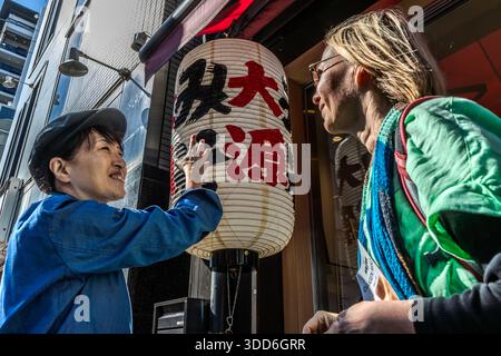 A shopkeeper explains to food journalist Angela Berg the paper lantern with red lettering outside a miso shop in Osaka, Japan. The characters ����Դ�� are written on the lantern. Stock Photo