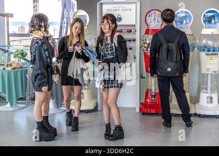 Three young women at a heart lock vending machine in the Umeda Sky Building, Osaka. Heart locks are also very popular in Japan, alongside the ubiquitous gachapon vending machines. Three young women and a man stand in front of vending machines in the Umeda Sky Building in Osaka, Osaka Prefecture, Japan Stock Photo