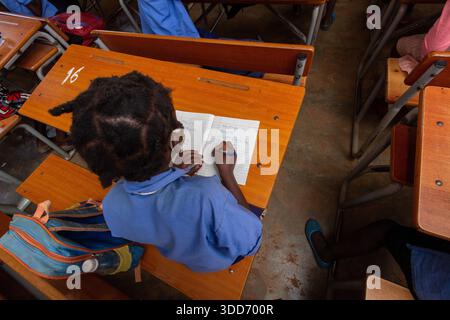 African Schoolgirl Writing in Exercise Book at Classroom Desk Stock Photo