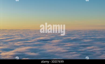 The view shows a wide sky above thick clouds. The colors change from blue to soft shades of yellow and orange. The moment seems fresh and new. In the Stock Photo