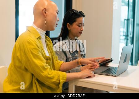 Diverse women collaborating on laptop, discussing work at modern office cafe Stock Photo