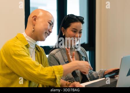 Two smiling diverse women working together on laptop, discussing business ideas in office Stock Photo