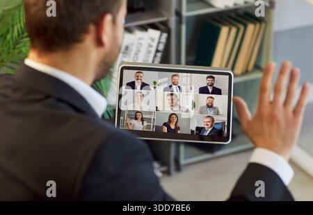 Entrepreneur having online meeting with remote business team and waving hand at tablet Stock Photo