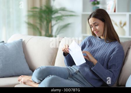 Frustrated woman preparing letter to send or receiving sitting on a sofa at home Stock Photo