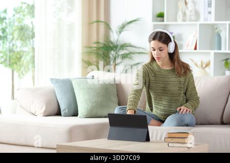 Woman wearing headphone preparing online content on tablet sitting on a sofa at home Stock Photo