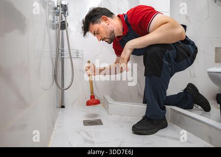 Plumber Using Plunger unclogging shower drain in bathroom Stock Photo
