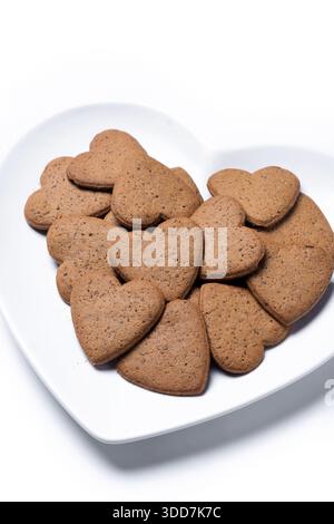 Heart-shaped gingerbread cookies on a white heart-shaped plate isolated on white background Stock Photo