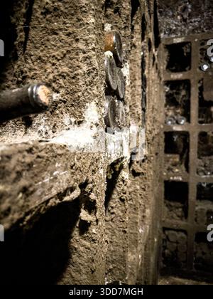 A detailed view of a textured stone wall adorned with embedded coins, set against a backdrop of a metal grate and a pipe. The image captures the uniqu Stock Photo