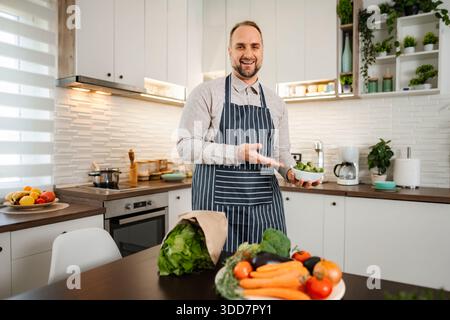 Man smiling holding fresh Brussels sprouts in kitchen Stock Photo